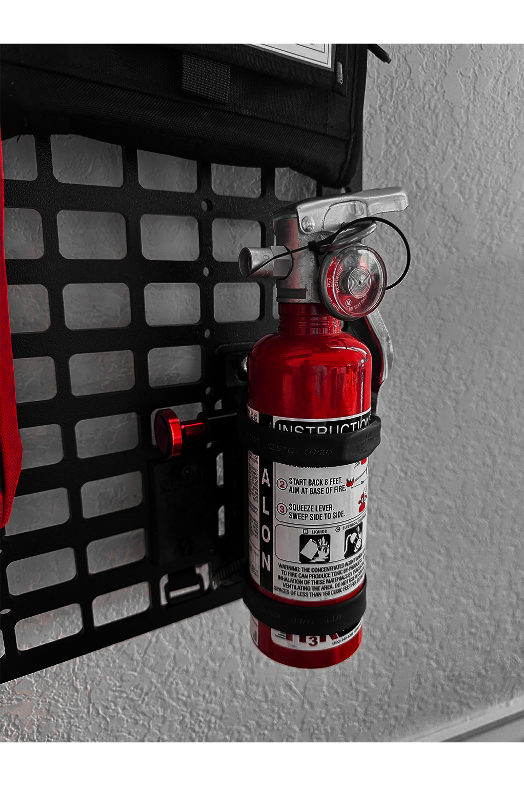 Red fire extinguisher mounted on a molle rack with a textured background