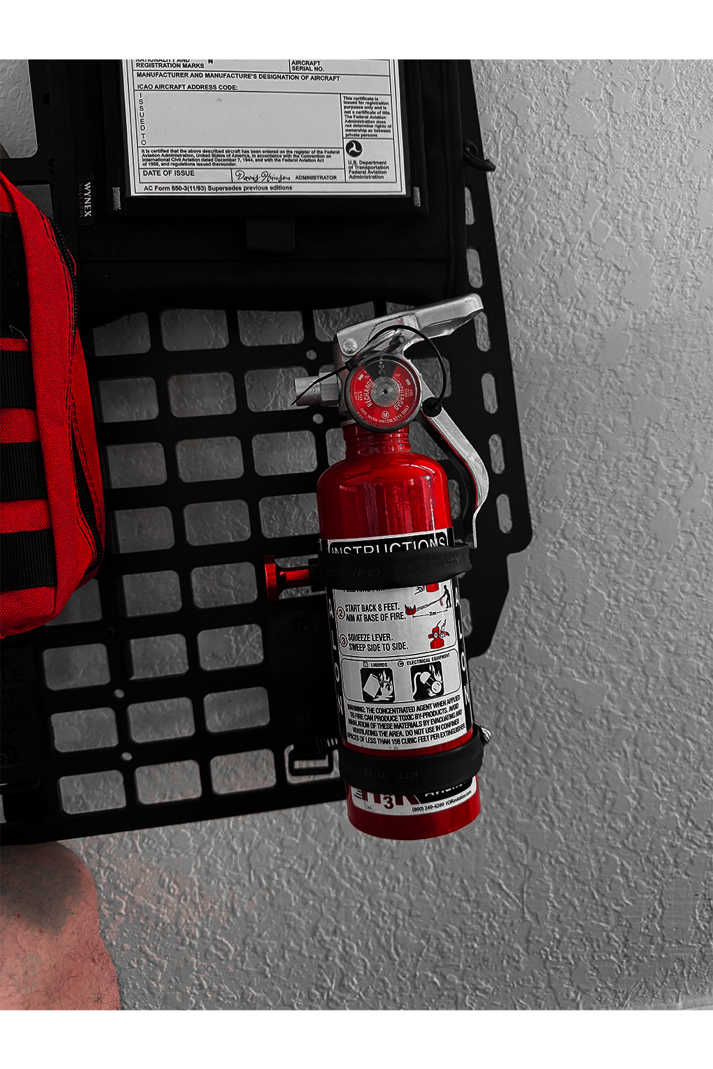 Red fire extinguisher mounted on a molle rack with a textured background