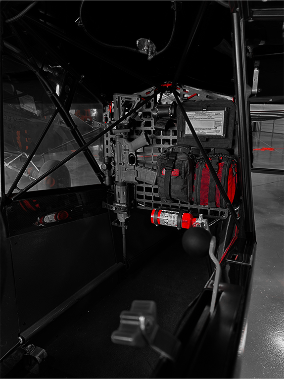 Dark interior of an aircraft with tactical bags and equipment attached to a Molle Rack.