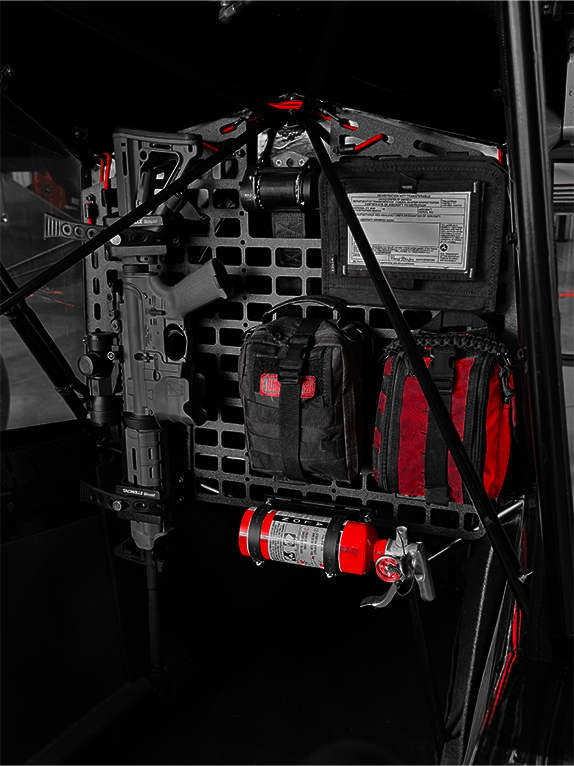 Dark interior of an aircraft with tactical bags and equipment attached to a Molle Rack.