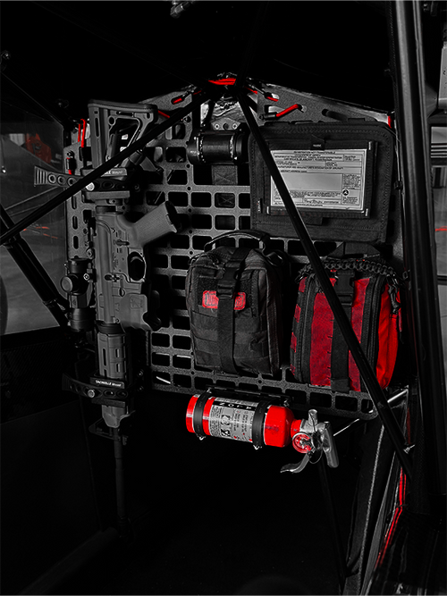 Dark interior of an aircraft with tactical bags and equipment attached to a Molle Rack.