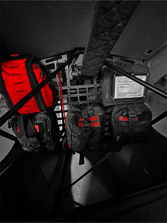 Red and black tactical bags attached to a Molle Rack inside an aircraft.