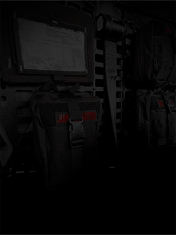 Dark interior of an aircraft with tactical bags and equipment attached to a Molle Rack.