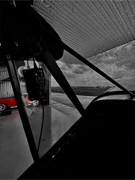 Black and white interior of an airplane cockpit with a red vehicle outside.